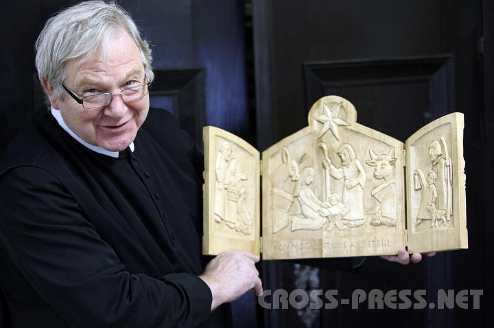 2009.12.03_11.17.20.jpg - P. Martin zeigt eine Besonderheit: seine "kleine Jahreskrippe", 2007 entstanden, deren Teile er jeweils beidseitig geschnitzt hat mit Szenen von der Verk�ndigung bis zur Himmelfahrt, wobei Geburt und Kreuzigung gro� dargestellt sind.